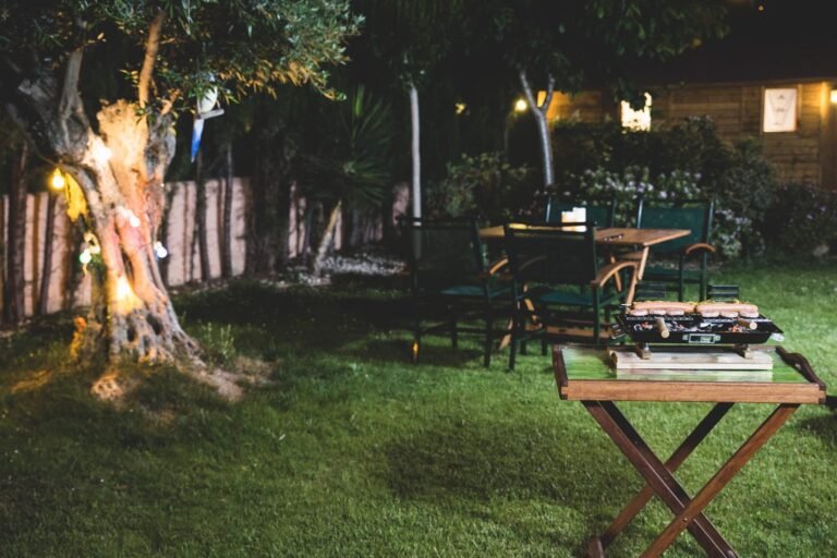 Área gourmet simples no jardim à noite, com mesa, luzes e churrasqueira