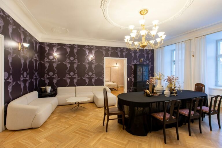 Sala ampla com papel de parede estampado em tom berinjela, sofá branco e mesa de jantar sob lustre