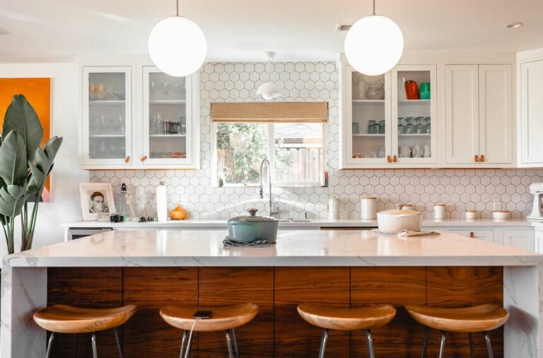 Cozinha clara com ilha de mármore, banquetas de madeira e revestimento hexagonal na parede